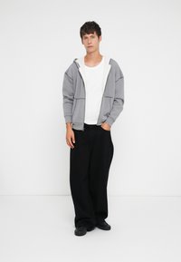 Pelēka kapuce ar rāvējslēdzēju un baltu iekšpusi, apvienota ar melniem brīvā griezuma biksēm un valkāta ar tumšām apaviem. Vienkāršs, ikdienišķs dizains.