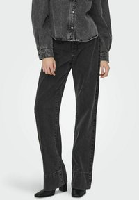 Jeans de mezclilla negra con un ajuste holgado, con cintura alta, piernas rectas y costuras en contraste. Llevados con botas de tacón negras.