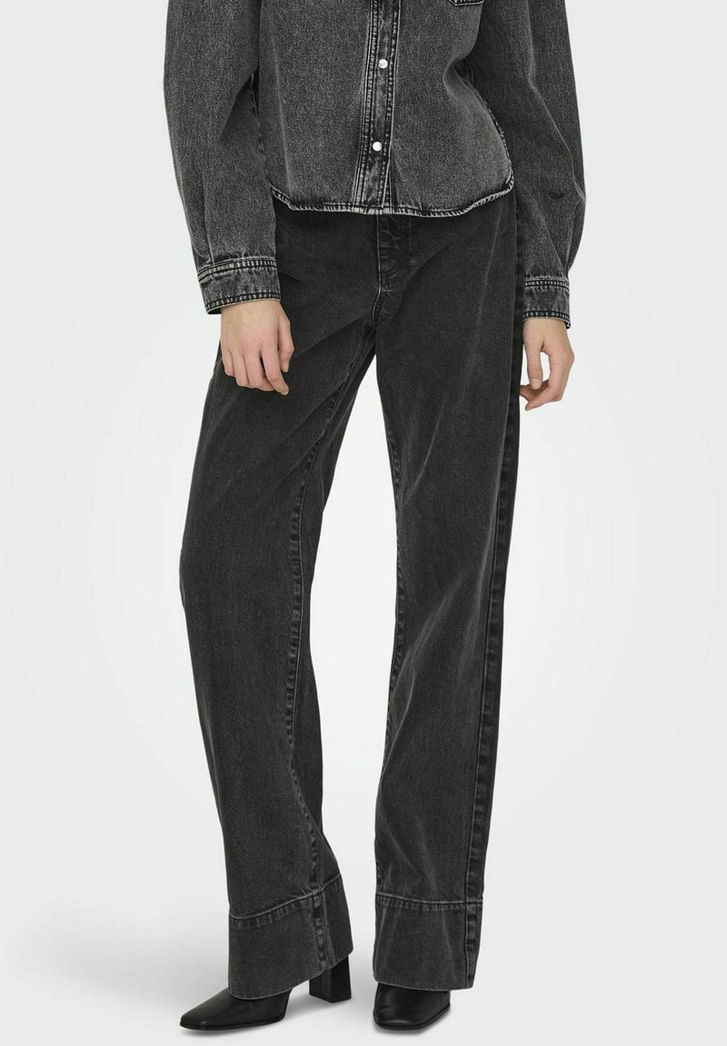 Jeans de mezclilla negra con un ajuste holgado, con cintura alta, piernas rectas y costuras en contraste. Llevados con botas de tacón negras.
