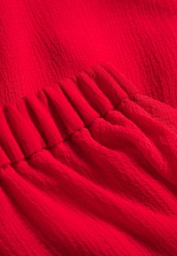 Gros plan d'un tissu rouge vif à surface texturée avec un détail élastique froncé créant des plis.