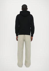 Felpa nera con cappuccio, dal taglio rilassato, abbinata a pantaloni larghi color beige chiaro, caratterizzati da un tessuto testurizzato e una palette di colori neutri.
