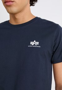 Marineblå bomull T-skjorte med rund hals, korte ermer, og en hvit "Alpha Industries" logo og design på venstre bryst.