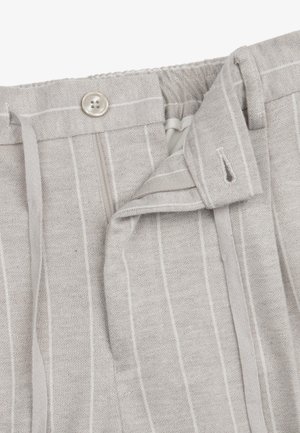Jasnoszare spodnie w cienkie prążki z zapięciem na guzik, zamkiem błyskawicznym i szlufkami na pasek, ukazujące częściowo otwartą talię.