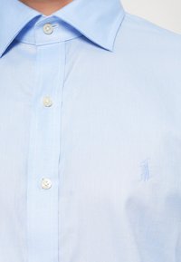 Světle modrá košile na knoflíky s texturovaným vzorem, klasickým límečkem, bílými knoflíky a jemným logem ve tkanině.