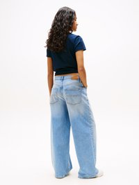Light blue wide-leg jeans made of denim, featuring subtle fading, back pockets, and a tan leather patch at the waistband, worn with a navy t-shirt.
