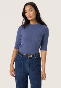 Ribbed knit, short-sleeved top in soft blue. Round neckline, fitted design. Paired with high-waisted denim and a brown belt with gold buckle.
