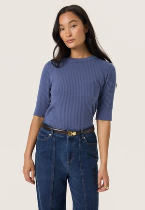 Ribbed knit, short-sleeved top in soft blue. Round neckline, fitted design. Paired with high-waisted denim and a brown belt with gold buckle.