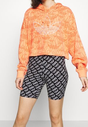 Hoodie orange court avec motif floral blanc en ligne et logo ; shorts noirs avec texte 'VANS' blanc répété et accents à damier.