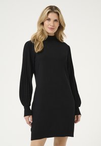 Schwarzes Strickkleid mit hohem Kragen, gerippten, plissierten langen Ärmeln und figurbetonter Silhouette, die oberhalb des Knies endet. Glatte Stofftextur.