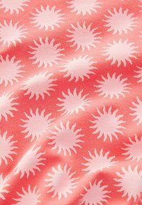 Tejido de color coral con una textura suave que presenta un patrón repetido de motivos de sol en tono rosa claro con rayos radiantes.