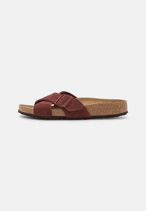 Sandale à glisser en suède marron avec un semelle en liège, dotée d'un large design de sangles croisées et d'une fermeture à boucle ajustable. Semelle en caoutchouc.