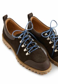 Scarpe in suede marrone con lacci blu, dettagli in metallo argentato e una suola in gomma con grip testurizzato. Accenti in pelle liscia sul tallone.