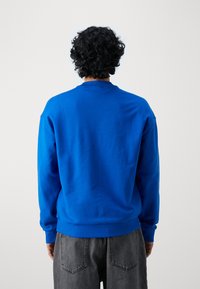 Blauwe sweatshirt met ronde hals, gemaakt van zachte stof, met ribgebreide manchetten en zoom. Draag het met grijze spijkerbroeken.
