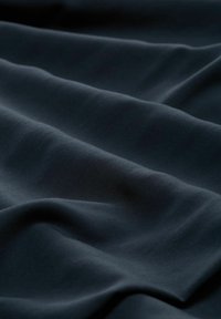 Dunkelblauem Stoff mit glatter Textur, der sanfte Wellen und subtile Falten aufweist, die das Licht sanft über seine Oberfläche reflektieren.