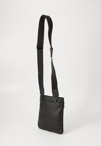 Črn usnjen torbica preko telesa z teksturirano površino, nastavljivim platnenim trakom in minimalističnim dizajnom. Vsebuje gladke kovinske dodatke.