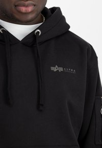 Hanorac negru cu glugă, fabricat dintr-un amestec de bumbac, având o buzunare frontală și un logo pe partea stângă a pieptului. Cordon și mansete răsucite.
