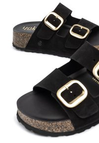 Sandali in suede nera con due larghe cinghie dotate di fibbie dorate. Suola intermedia in sughero e suola in gomma nera testurizzata. Logo del marchio dorato sulla plantare.