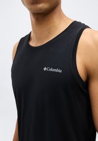 Άνδρας που φοράει μαύρο αθλητικό φανελάκι Columbia χωρίς μανίκια, εμφανίζοντας το στήθος, τον λαιμό και τον δεξί ώμο, πάνω σε απλό φόντο.