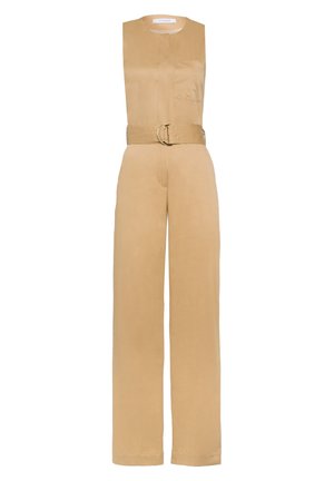 Hihaton beige haalari, jossa edessä tasku ja solmittu vyö, päällä oranssit remmillä varustetut lohkokorkoiset sandaalit, seisovalla henkilöllä.
