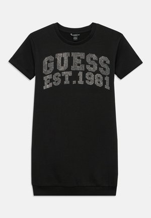 Vestido negro de manga corta con la inscripción "GUESS EST. 1981" en letras blancas punteadas en el pecho.