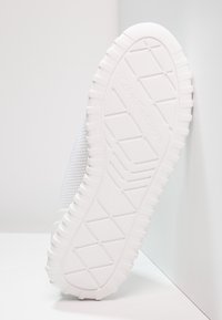 Vit sneakers med ett strukturerat nätövre och en tjock, mönstrad gummisula. Logotyp präglad på sulan. Minimalistisk design, inga synliga accenter.