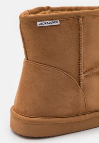 Brune semsket ankelstøvel med myk tekstur, forsterkede sømmer og et stoffmerke merket "JACK&JONES." Flat gummisåle uten synlige mønstre.