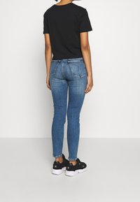 Czarny bawełniany t-shirt, niebieskie obcisłe dżinsy i czarne sneakersy. Dżinsy mają klasyczny krój z detalicznym przeszyciem na tylnych kieszeniach.