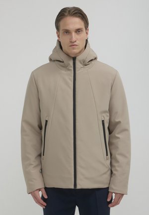 Veste à capuche beige avec une texture lisse, fermeture éclair noire, poches latérales et un design épuré. Présente des coutures en relief pour un détail supplémentaire.