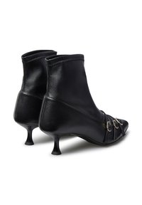 Stivali alla caviglia in pelle nera con punta affusolata, tacco sottile e catene decorative sul davanti. Textura liscia con dettagli cuciti.