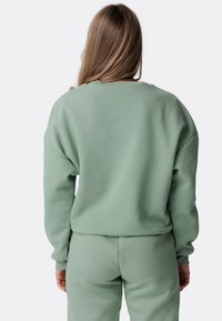 Felpa over-size verde chiaro con maniche lunghe, polsini a coste e scollatura rotonda, abbinata a pantaloni jogger coordinati per un look coeso.