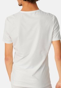 T-shirt blanc à manches courtes avec un col rond, texture lisse et subtils motifs rayés verticaux. Vue de dos montrant une coupe décontractée et la simplicité.