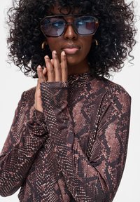 Długi rękaw, top w wzór wężowej skóry w odcieniach brązu i beżu. Posiada wysoki kołnierz i dopasowany krój, wykonany z lekkiego, elastycznego materiału.