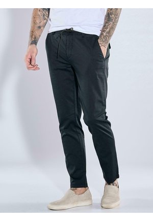 Schwarze tapered Hosen aus leichtem Stoff mit einem Kordelzugbund, seitlichen Taschen und einer glatten Textur, kombiniert mit hellen Schuhen.