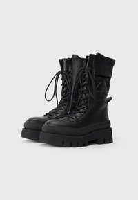 Schwarze Lederkampfstiefel mit einer massiven Gummisohle, Schnürverschluss und umgeschlagenem Design. Enthält Nähdetails und eine Zuglasche.