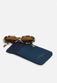 Runda sköldpaddsögon med bruna linser som vilar på ett mjukt navyblått fodral med "Le Specs". Fodralet har en slät yta.