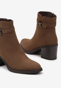Bottines en suede marron avec un talon carré, dotées d'une sangle décorative et d'un accent de boucle. Texture lisse et design à bout rond.
