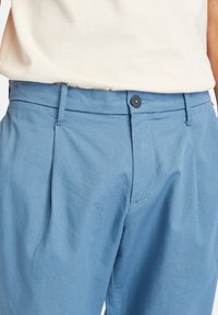 Niebieskie spodnie z mieszanki bawełny z płaskim przodem, pojedynczym zapięciem na guzik i szlufkami na pasek. Gładka tekstura i dopasowany krój widoczny na wysokości talii.