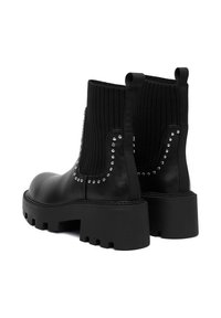Czarne botki za kostkę z okrągłym noskiem, ryflowanym materiałem na górze, akcentami w postaci ćwieków i grubą podeszwą. Gładka skórzana powierzchnia z teksturowanym wykończeniem.