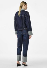 Tummansininen farkkutakki ja housut yhdistelmä rakenteellisella muotoilulla. Takissa on harmaa kaulus, ja housuissa on risaiset harmaat lahkeet.