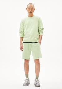 Lichtgroene sweatshirt en bijpassende shorts van zachte stof. De sweatshirt heeft een ronde hals; de shorts hebben een elastische tailleband en zakken.