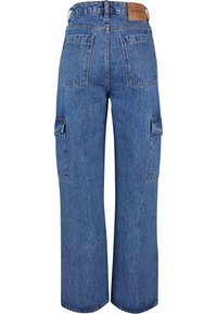 Jean en denim bleu à jambes larges avec poches plaquées arrière, poches cargo latérales, passants de ceinture et un patch de marque en cuir marron sur la taille.