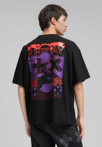 T-shirt nera oversize con una grafica colorata sul retro con testo "REPLAY", accenti in contrasto di viola e arancione, e design astratti.