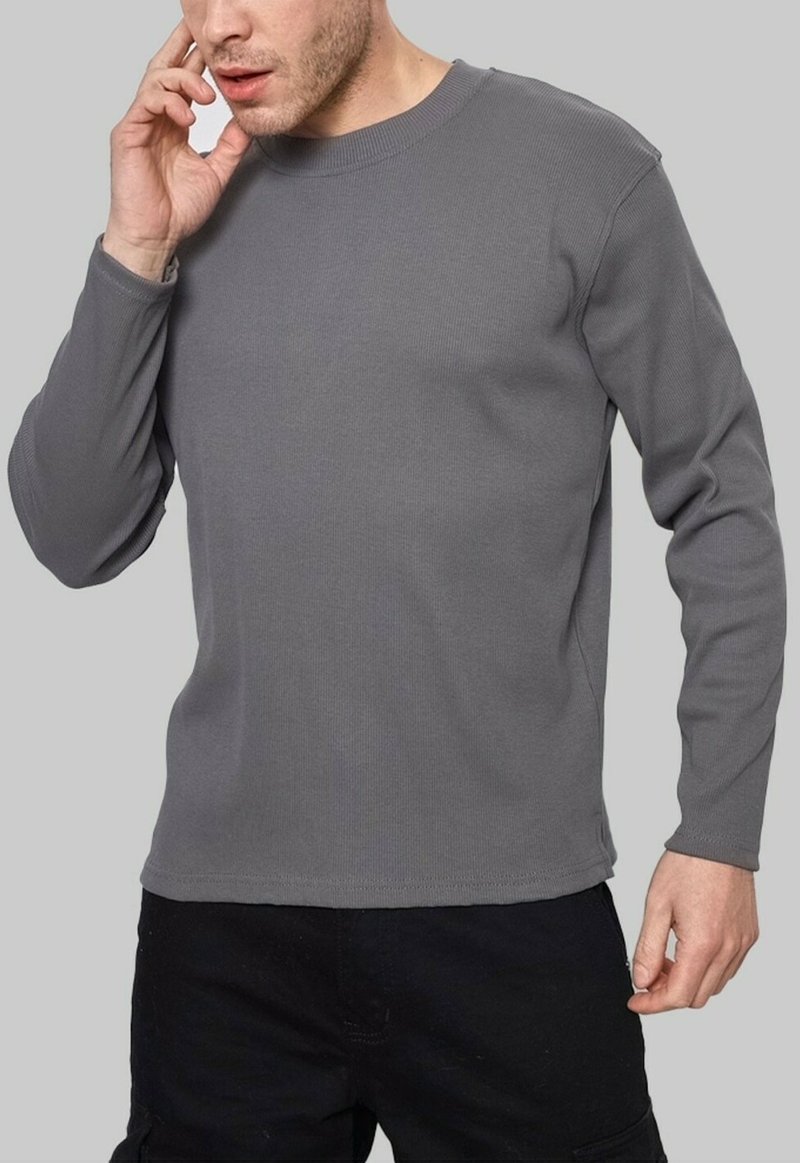T-shirt gris à manches longues en tricot côtelé avec un col rond et une coupe décontractée, offrant une texture douce et des coutures minimales pour un maximum de confort.