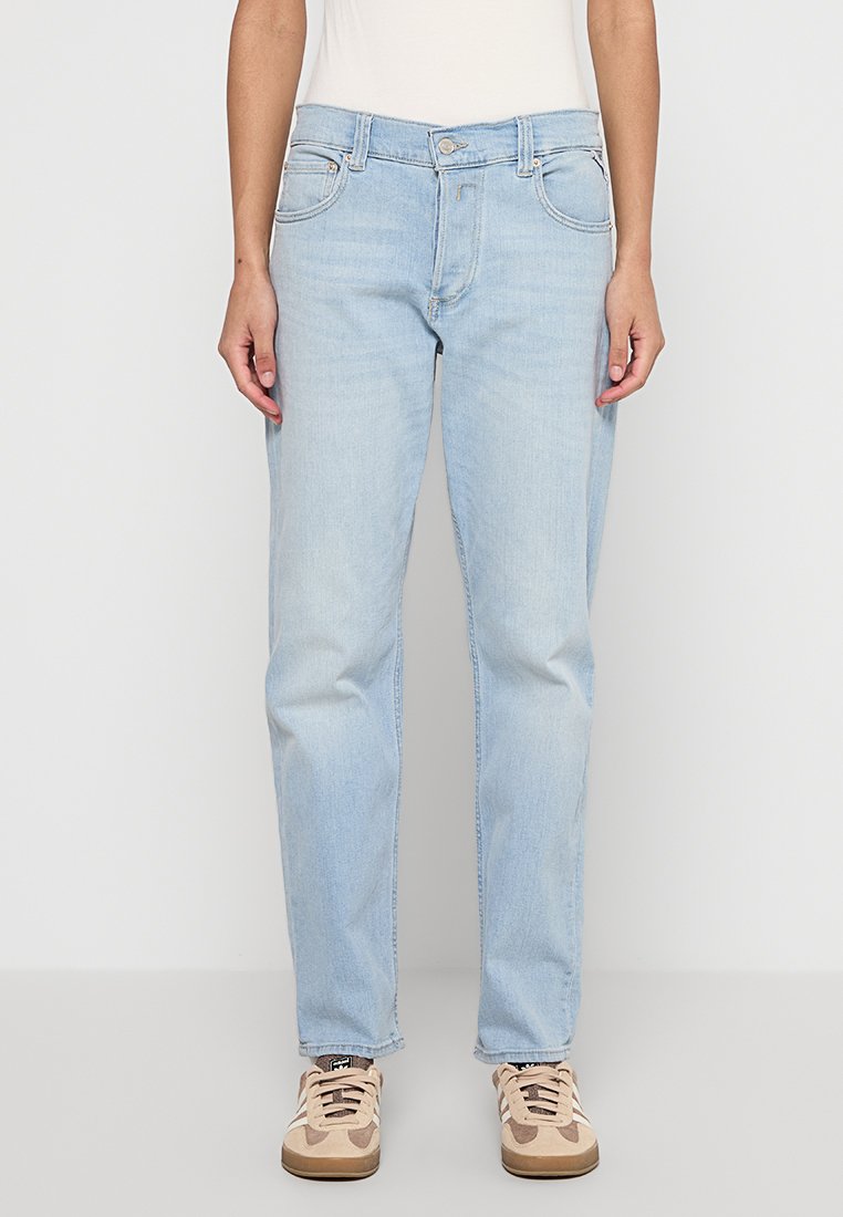 Helleblaue Denim-Jeans mit geradem Schnitt, fünf Taschen und einem Knopfverschluss. Getragen mit beigen Turnschuhen, die ein Schnürdesign und subtile Muster aufweisen.