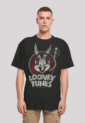 Fekete pamut póló, amelyen egy fejhallgatós Bugs Bunny grafika található, piros körben. A felirat: "Looney Tunes" elhasználódott fehér színben.