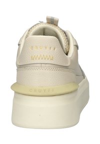 Crème-kleurige sneaker met een leren bovenwerk met textuur, een zachte kraag en een rubberen zool met goudkleurige logo-details op de hiel.