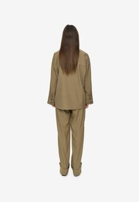 Conjunto de dos piezas en color beige que incluye una camisa de corte cuadrado y holgada, junto con pantalones de pierna ancha, ambos en tejido texturizado y con puños enrollados.