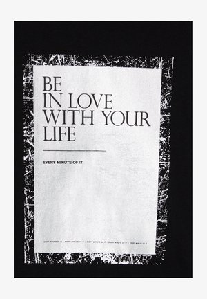 Czarna bawełniana koszulka z dużym białym prostokątnym graficznym nadrukiem z tekstem: "Kochaj swoje życie każdą minutą!" oraz postarzonym obramowaniem.