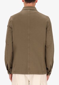 Giacca verde oliva con colletto, taglio dritto, polsini abbottonati e texture liscia. Presenta una cucitura centrale e tasche laterali.