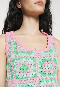Crochet tank top featuring a scalloped neckline and a diamond pattern in pink, green, and light blue. Made of soft yarn with a textured finish.